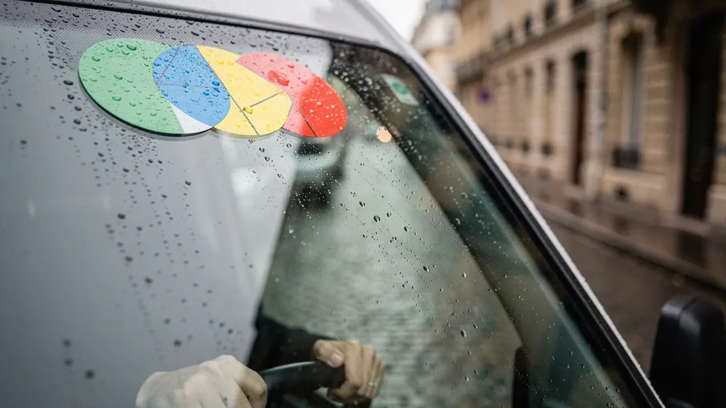 Gros plan sur le pare-brise d'un véhicule utilitaire avec des vignettes colorées floues collées, dans un contexte urbain français